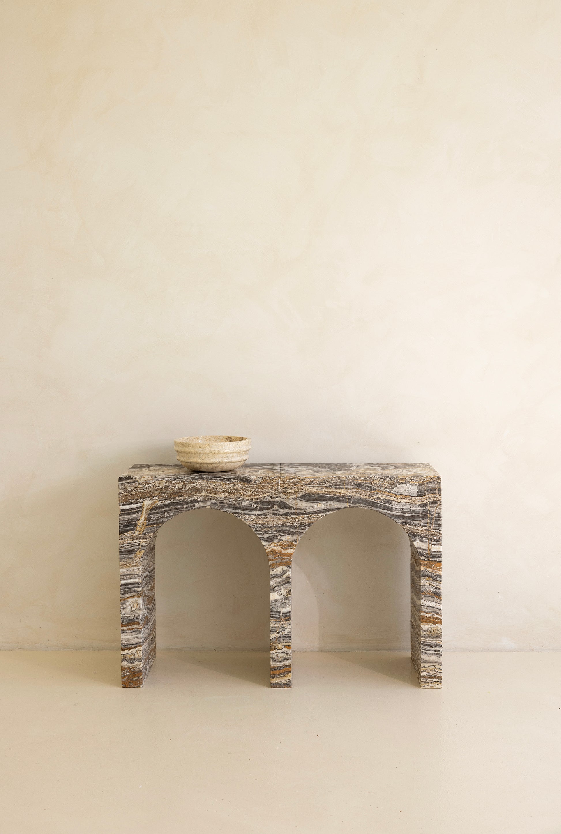 A marble console table with twin arches and a dramatic stone pattern against a neutral background.