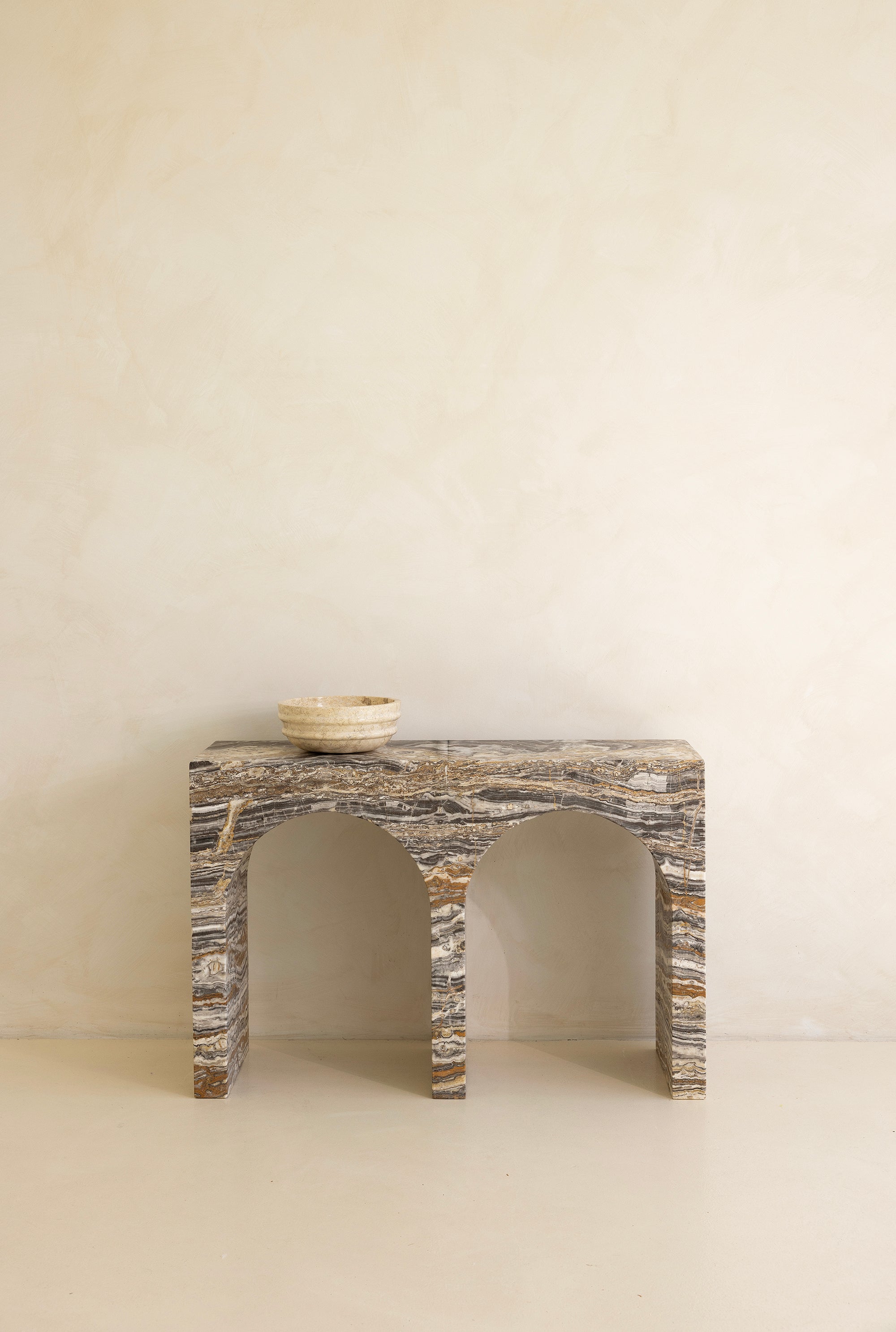A marble console table with twin arches and a dramatic stone pattern against a neutral background.