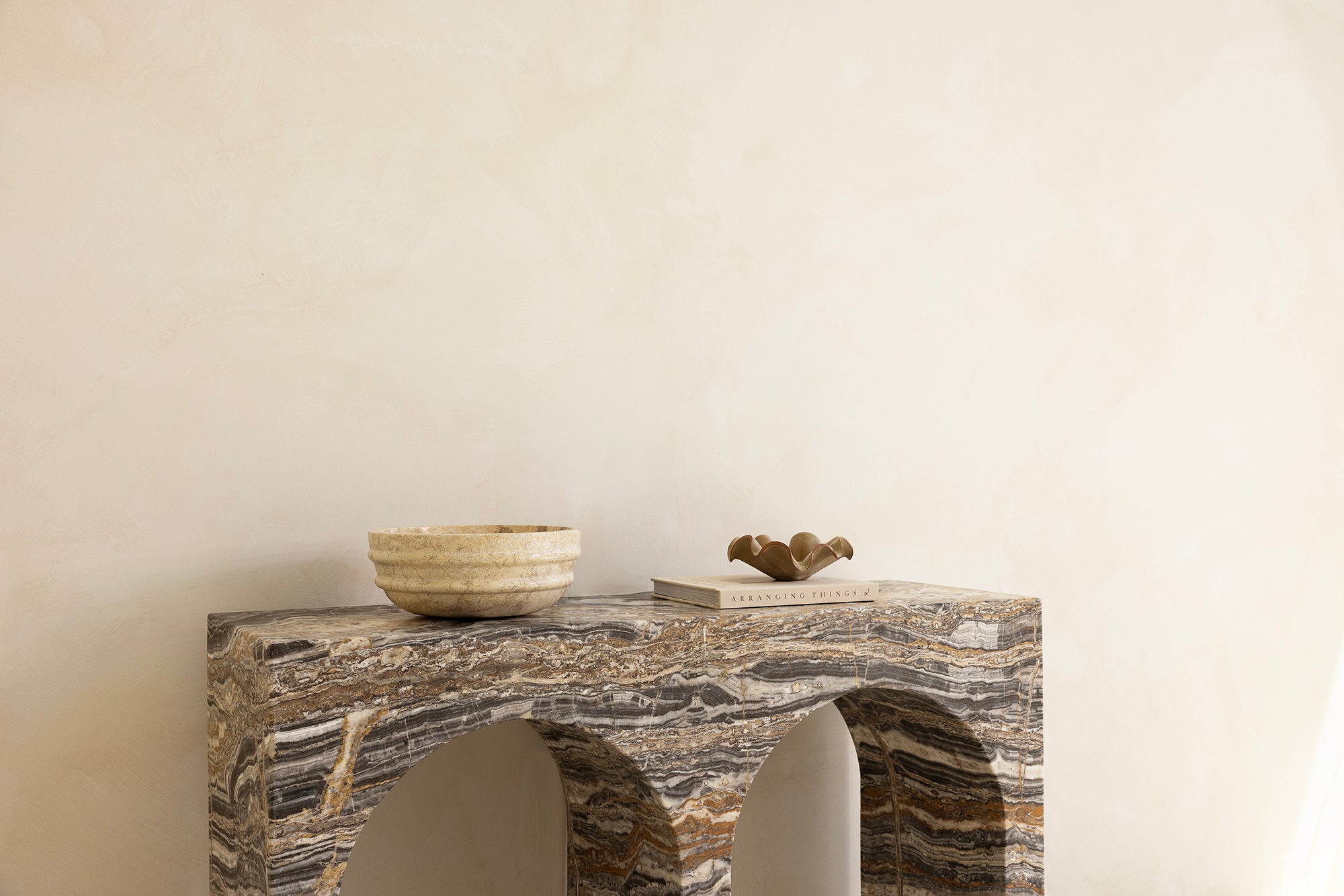 A marble console table with twin arches and a dramatic stone pattern against a neutral background.